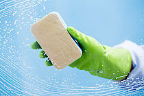 Eine Hand mit grünem Handschuh, die mit einem Schwamm eine Scheibe putzt