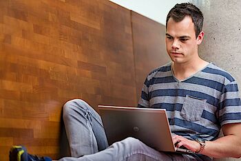 Ein Mann sitzt mit Laptop auf den Beinen vor einer Holzwand
