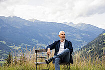Matthias Horx sitzt auf einem Stuhl, hinter ihm die Berge