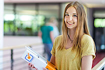 Eine lächelnde junge Frau mit einem ELBCAMPUS-Ordner in der Hand