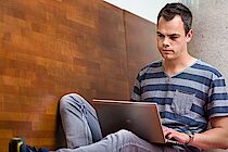 Junger Mann sitzt mit Laptop auf einer Bank